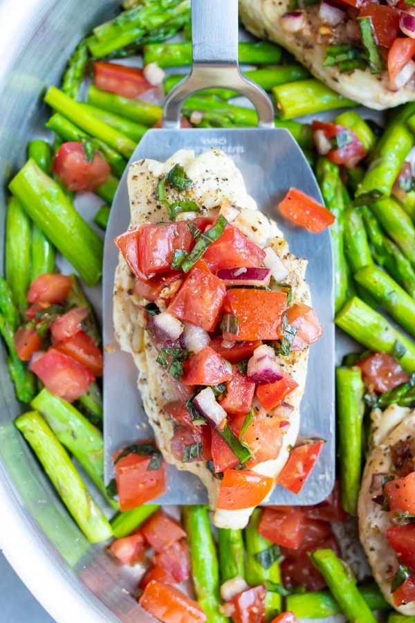 A quick, easy, and healthy bruschetta chicken recipe with asparagus in a stainless steel skillet with a spatula.