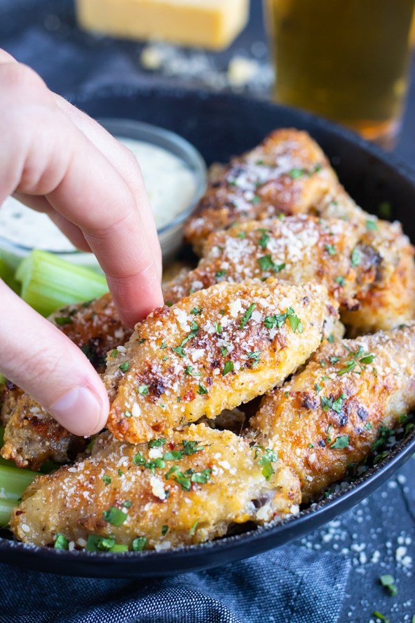 A hand picking up a baked wing from a serving bowl at a Super Bowl party.