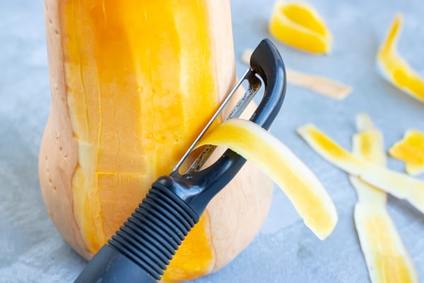 Peeling butternut squash with a vegetable peeler.