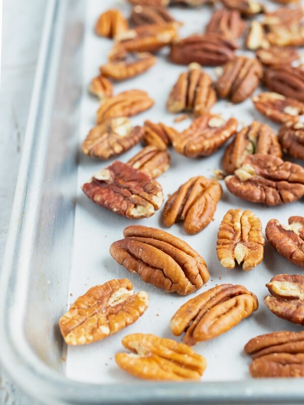 Toasted pecans on a large baking sheet that are going to be roasted in the oven.