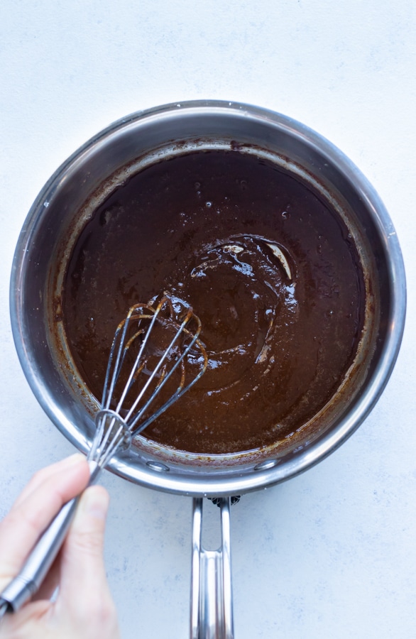 Dark brown roux is stirred with a whisk on the stove.