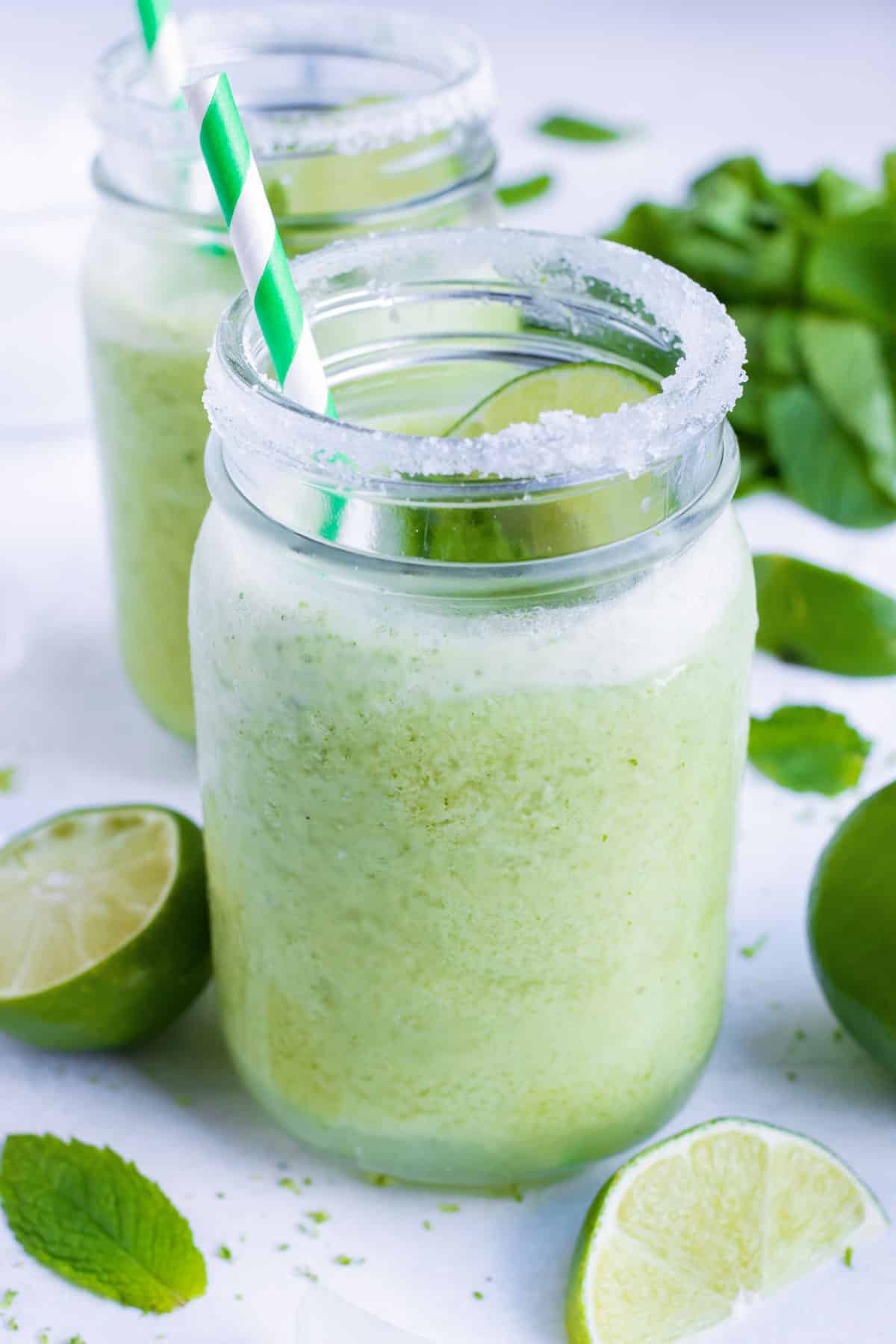A frozen mojito cocktail with limes around it.