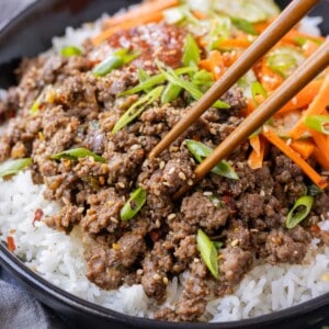 Korean beef is served in a black bowl with rice and pickled veggies.