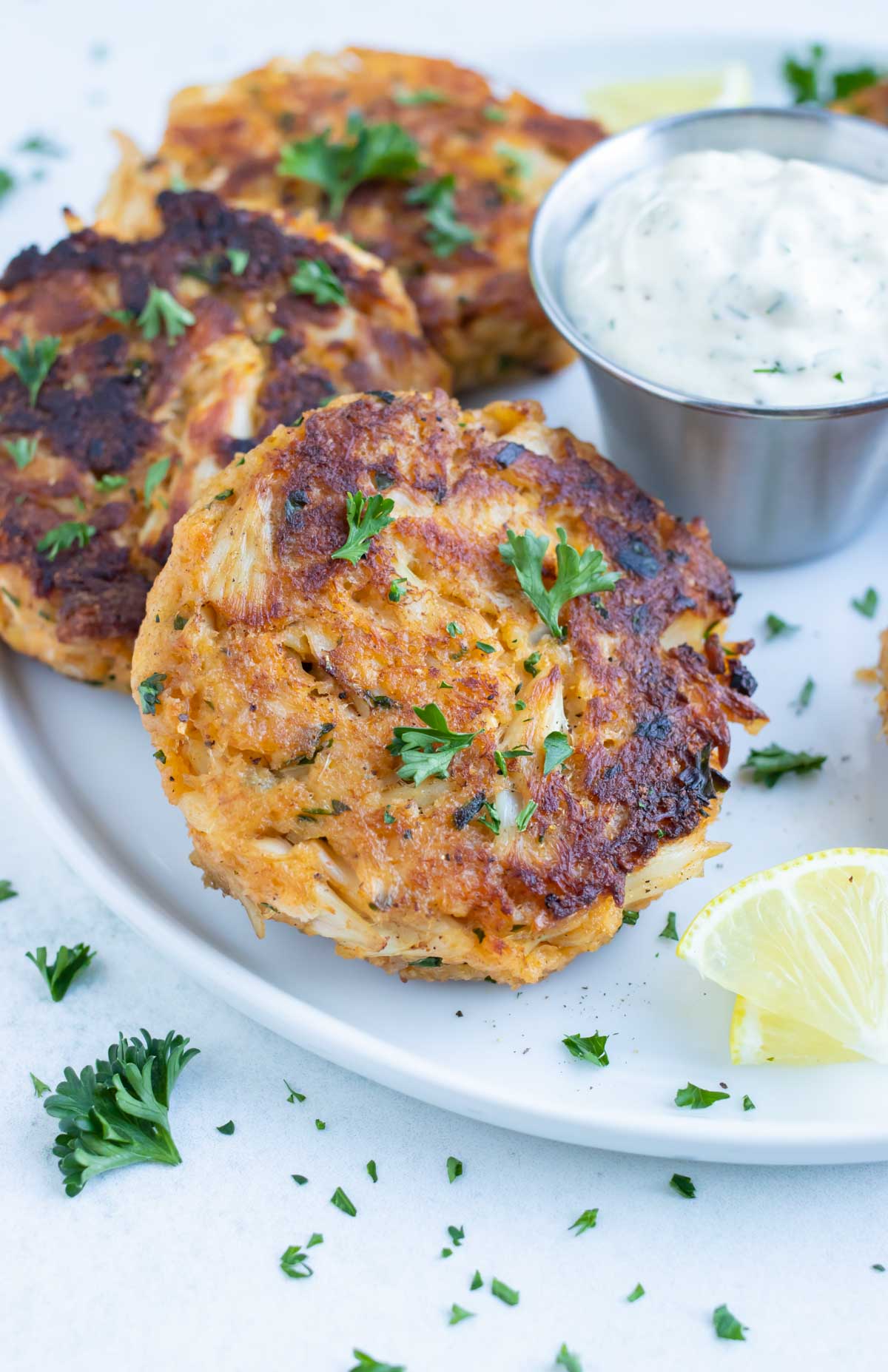 Homemade crab cakes are served on a white plate with fresh lemon and tartar sauce.