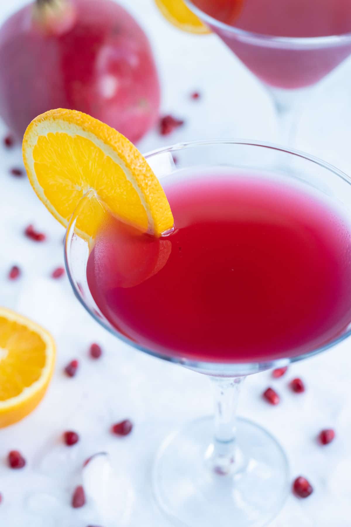 Beautiful pomegranate martini is shown garnished with a fresh orange slice.