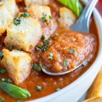 A spoon scooping out a bite of a thick and creamy roasted tomato soup recipe.