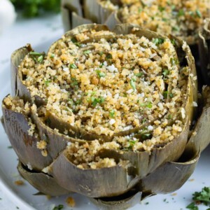 Oven-baked Italian stuffed artichokes are served on a white plate for a holiday appetizer.