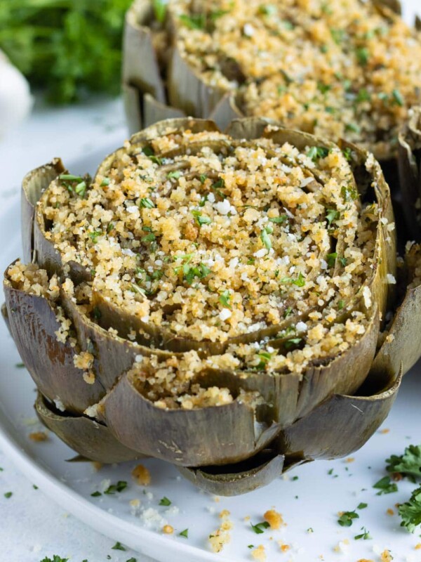 Oven-baked Italian stuffed artichokes are served on a white plate for a holiday appetizer.