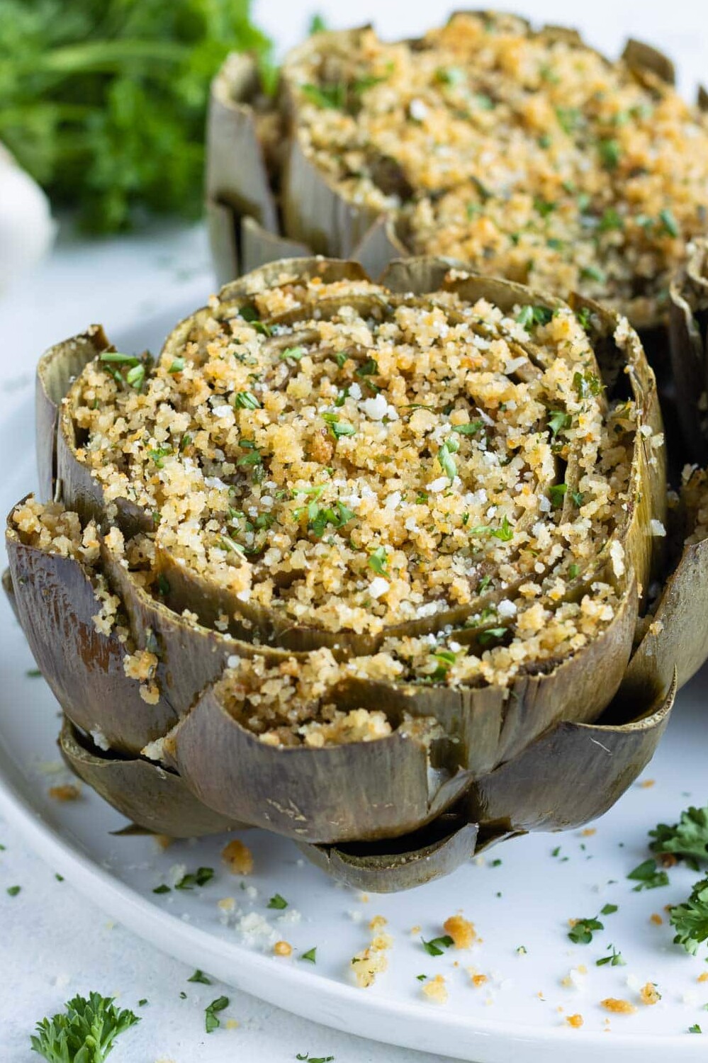 Oven-baked Italian stuffed artichokes are served on a white plate for a holiday appetizer.