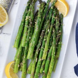 Air fryer asparagus are on a white plate with lemon wedges.