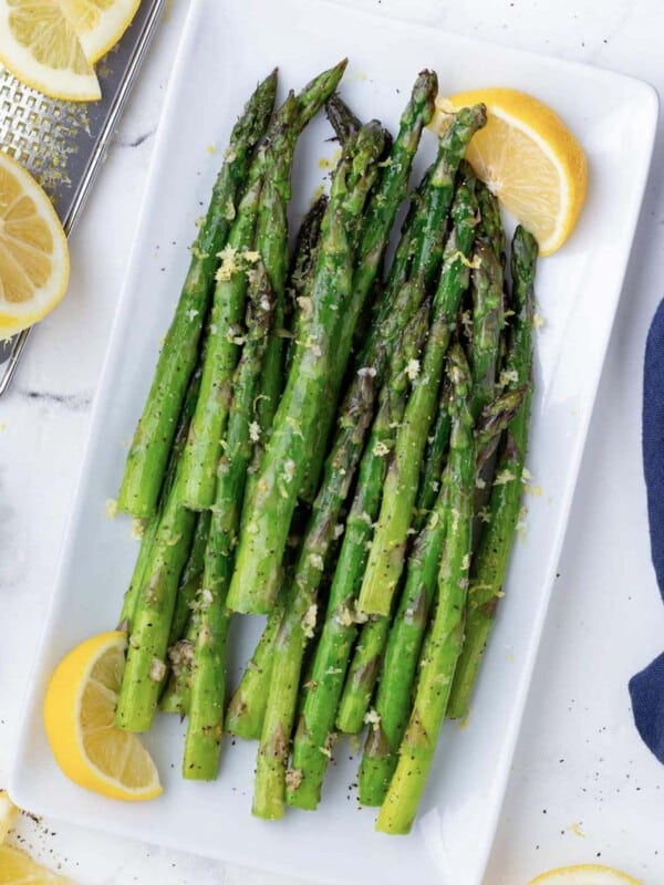 Air fryer asparagus are on a white plate with lemon wedges.