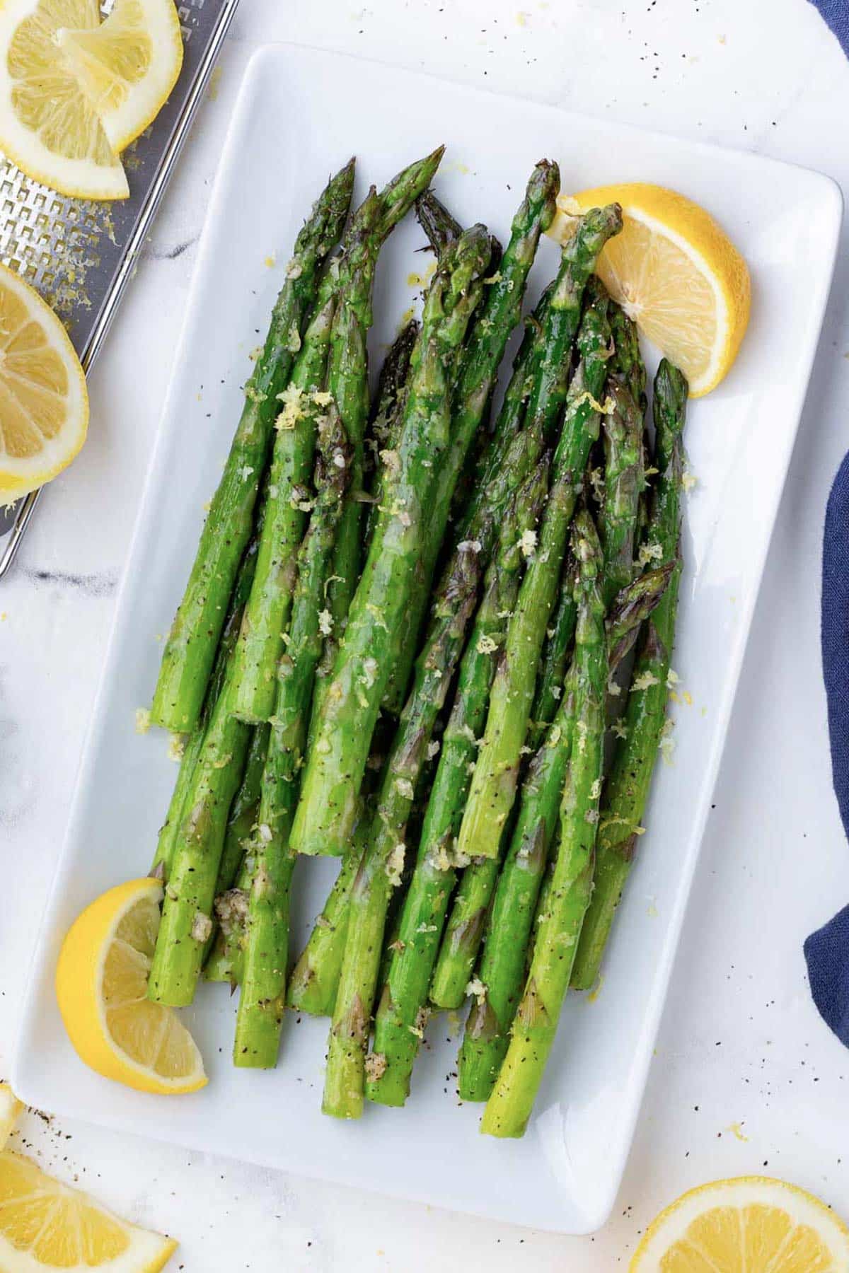 Air Fryer Asparagus RECIPE served on a white plate with a lemon wedge and lemon zest.