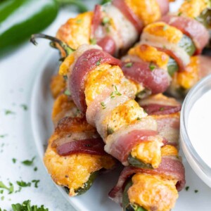 Bacon wrapped poppers are served on a plate with dip.