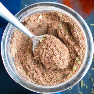 A silver spoon scooping out some homemade Cajun seasoning mix from a glass jar.