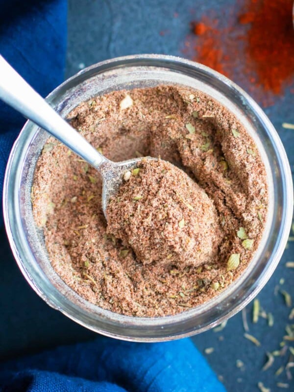 A silver spoon scooping out some homemade Cajun seasoning mix from a glass jar.