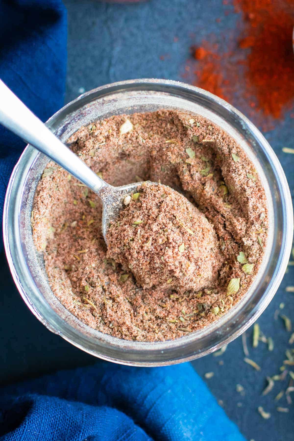 A silver spoon scooping out some homemade blackened seasoning mix from a glass jar.