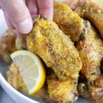 A hand is shown picking up a crispy lemon pepper chicken wing.