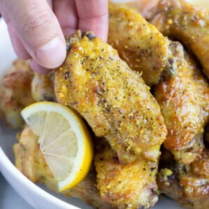 A hand is shown picking up a crispy lemon pepper chicken wing.