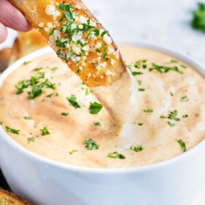 A baked potato wedge being dipped into a bowl full of Cajun remoulade sauce.