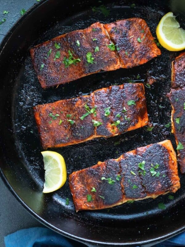 Cajun blackened salmon fillets in a cast-iron skillet with lemon wedges.