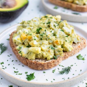 Avocado egg salad sandwiches are served on white plates.