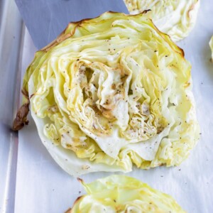 Roasted cabbage steak are lifted off a sheet pan by a spatula.