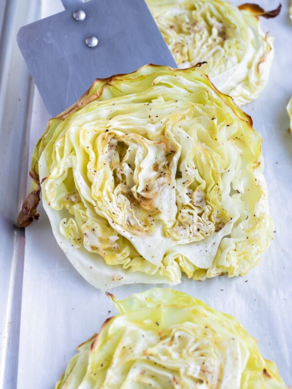 Roasted cabbage steak are lifted off a sheet pan by a spatula.