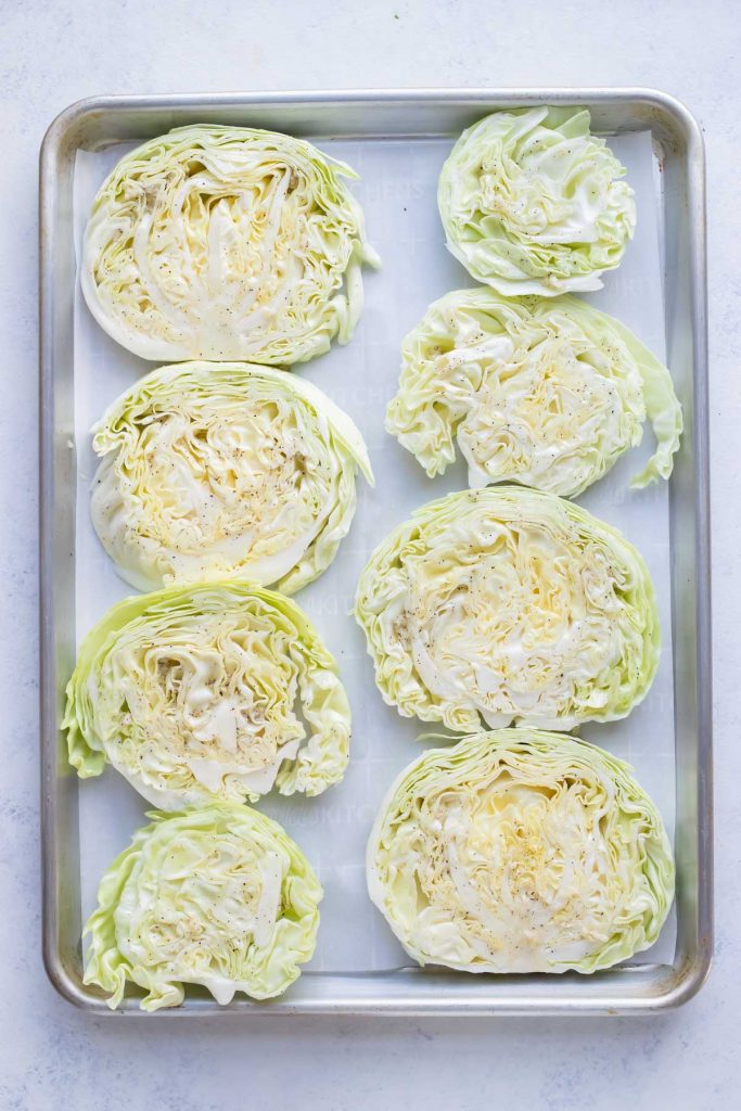 Cabbage steaks are laid flat on a baking sheet before roasting in the oven.