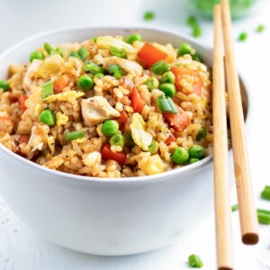 A white bowl full of a healthy fried rice recipe with carrots and peas next to green onions.