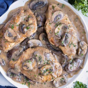 An Olive Garden Chicken Marsala copycat recipe is being served on a white plate next to a blue napkin.