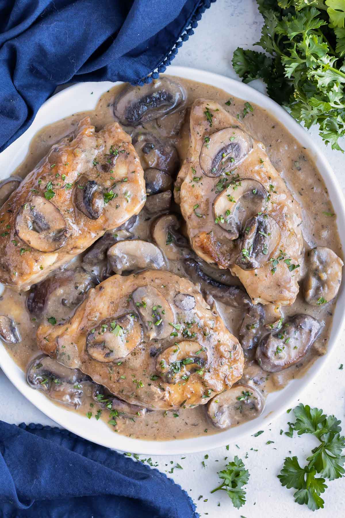 An Olive Garden Chicken Marsala copycat recipe is being served on a white plate next to a blue napkin.