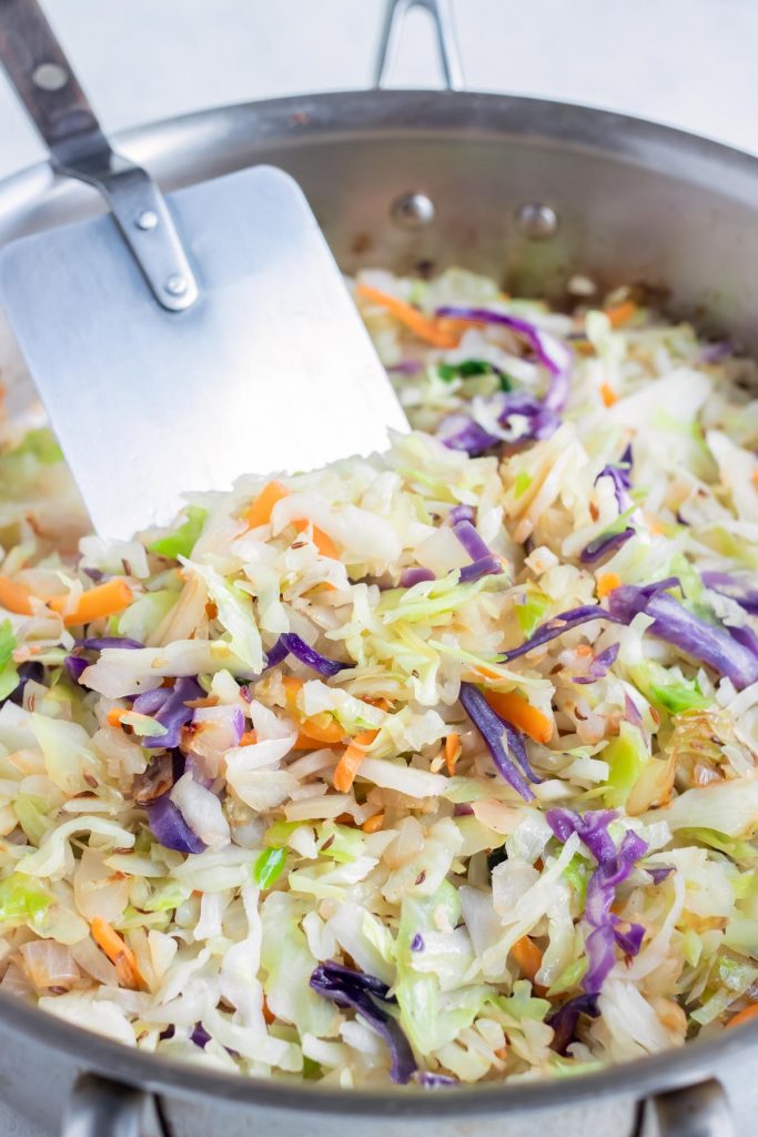 The shredded cabbage is sautéed on the stove.