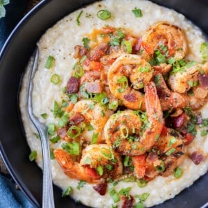 New Orleans Shrimp and Grits is served in a black bowl with green onions and parsley on top.