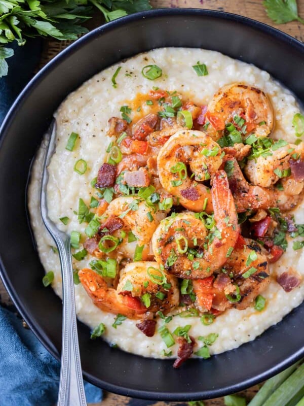 New Orleans Shrimp and Grits is served in a black bowl with green onions and parsley on top.