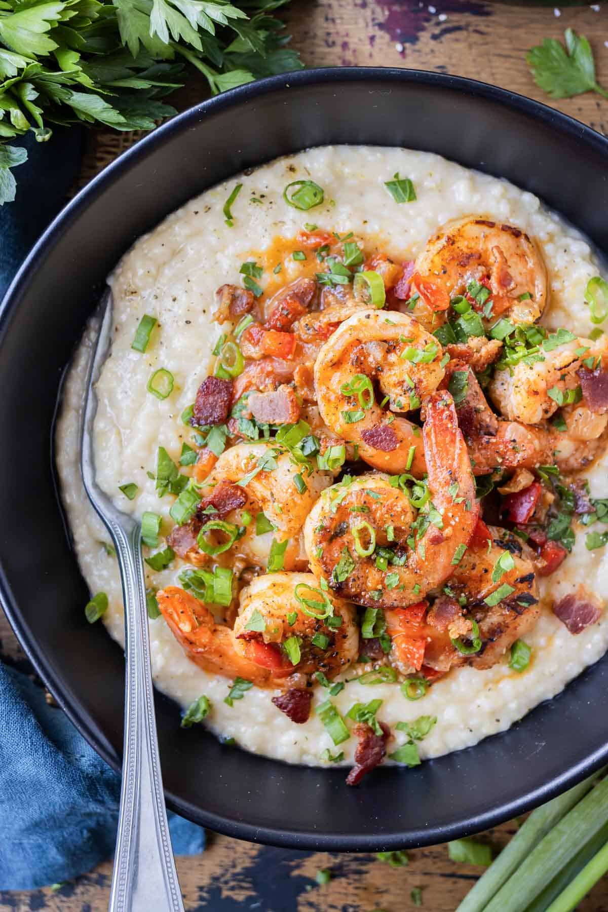 New Orleans Shrimp and Grits is served in a black bowl with green onions and parsley on top.