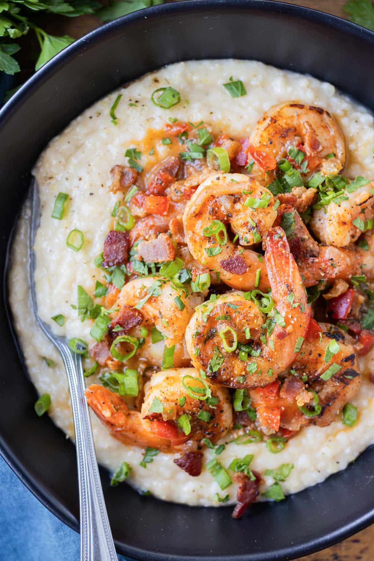 Shrimp are seasoned with Cajun flavors and served atop classic grits in a black bowl.