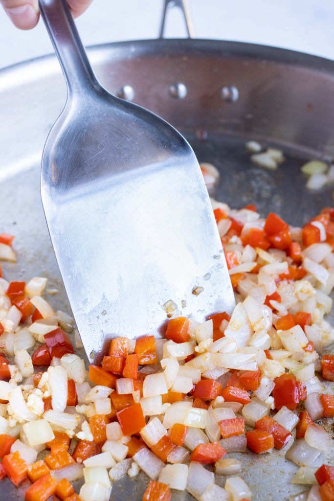 Diced onions and bell peppers are cooked in a pan.