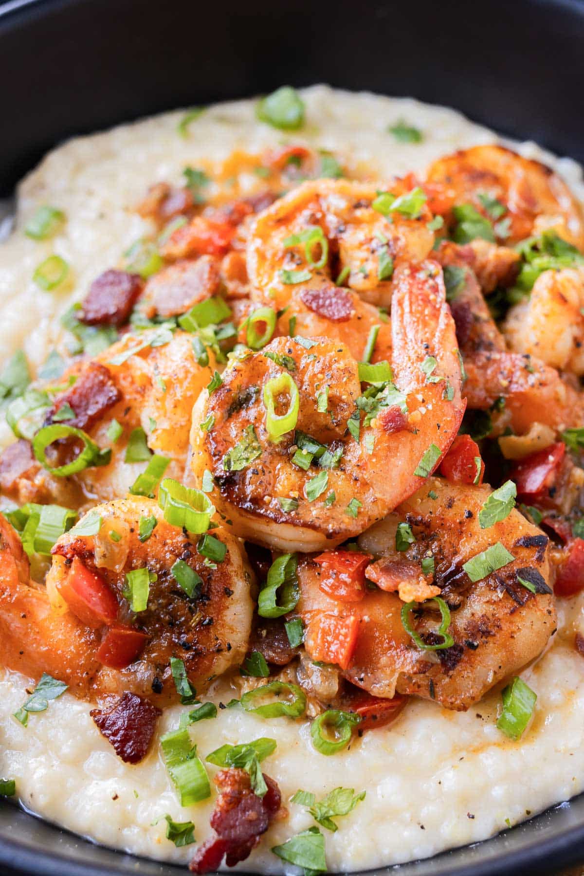 Seared blackened Gulf shrimp are served on top of creamy and cheesy grits in a black bowl.