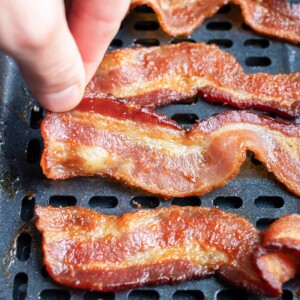 A slice of bacon is taken out of the air fryer after cooking.