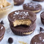 Two peanut butter cups are shown beside a bowl of peanut butter.