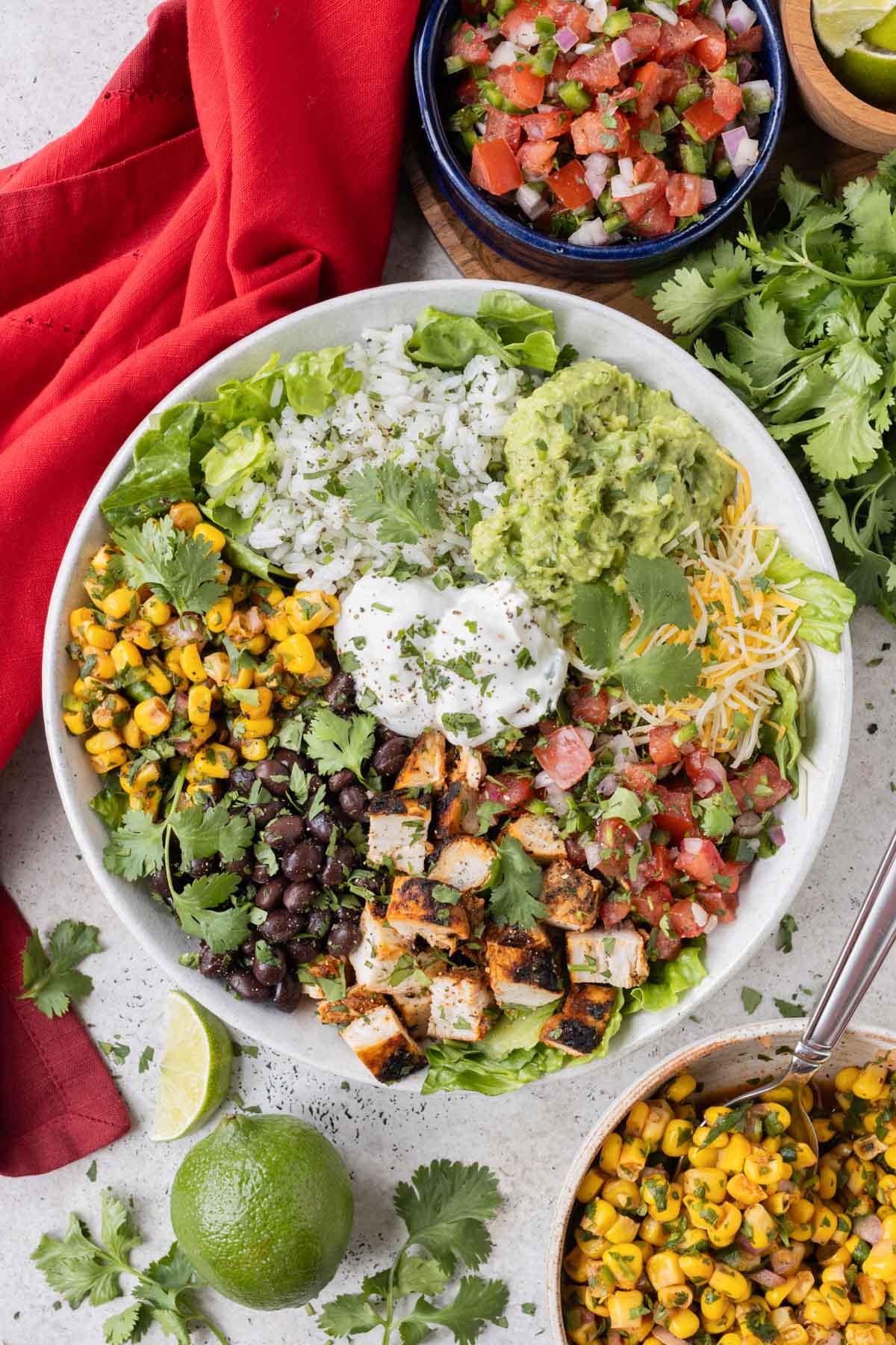 A white bowl is full of a Chipotle Burrito Bowl made at home with cilantro lime rice, Chipotle corn salsa, black beans, guacamole, and Chipotle chicken.