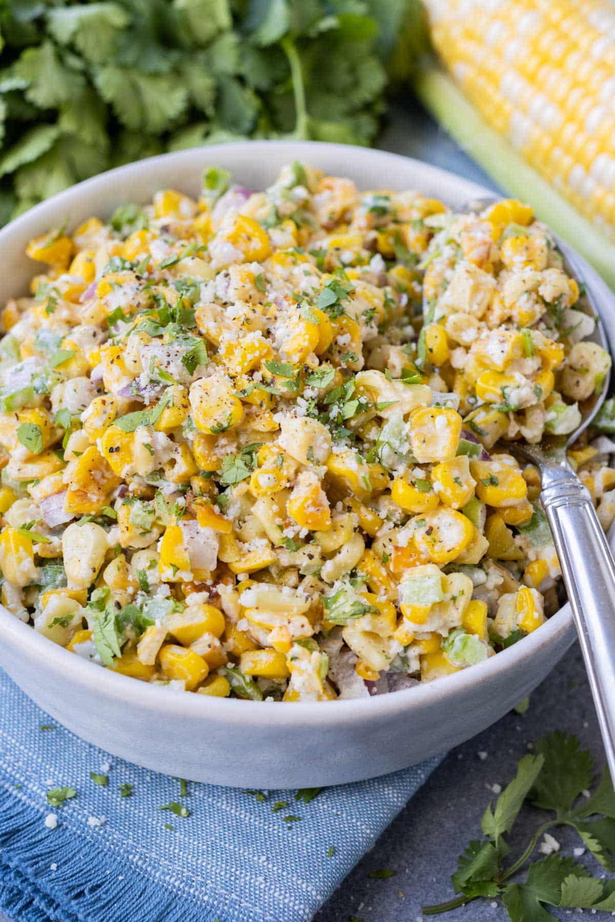 Mexican corn salad with fresh cilantro and Cotija cheese in a large white bowl with a spoon.