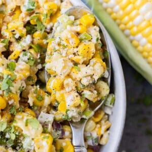 Mexican corn salad with fresh cilantro and Cotija cheese in a large white bowl with a spoon.