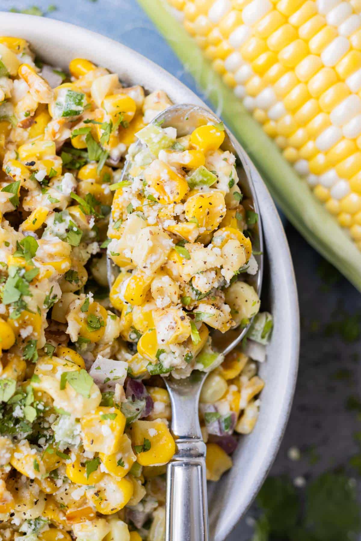 Mexican corn salad with fresh cilantro and Cotija cheese in a large white bowl with a spoon.