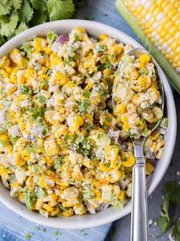 Mexican corn salad with fresh cilantro and Cotija cheese in a large white bowl with a spoon.