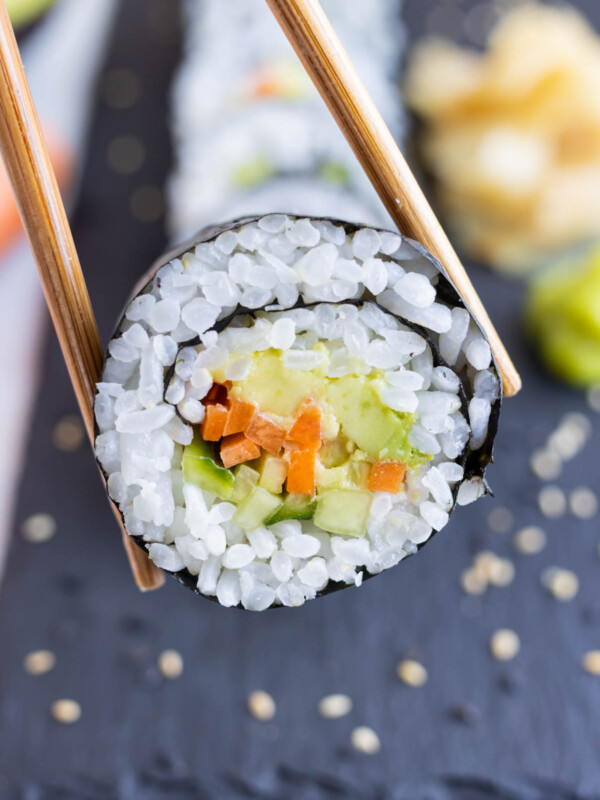 An avocado sushi roll is lifted up with chopsticks from the counter.