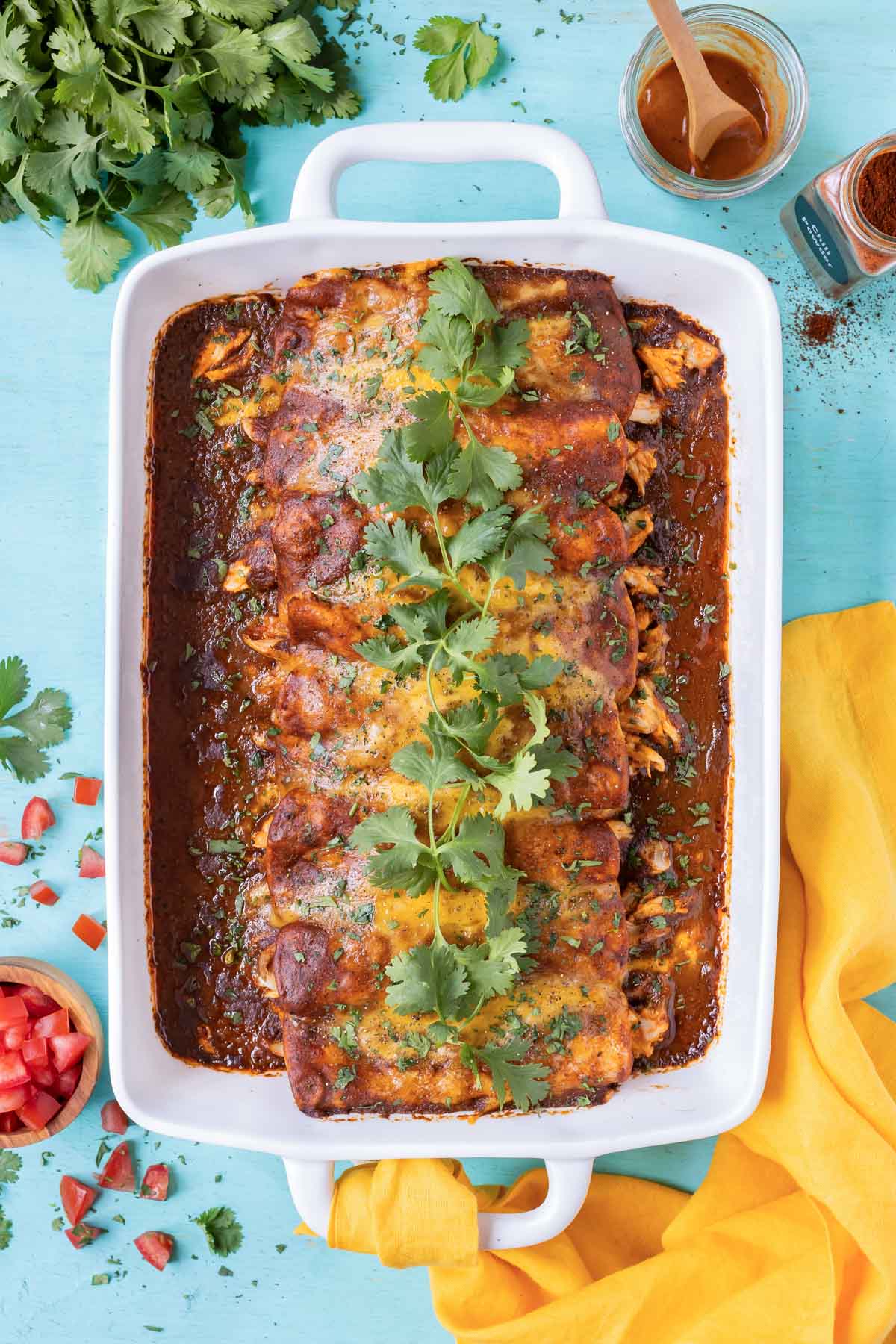 A dish full of shredded chicken enchiladas with cheese and a homemade sauce.