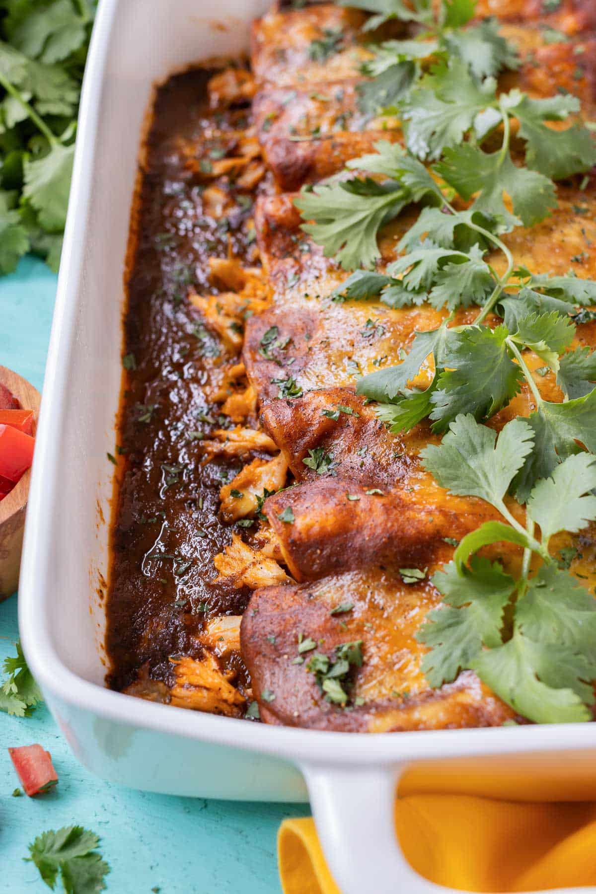 Chicken and cheese enchiladas in a baking dish with red sauce and cilantro.