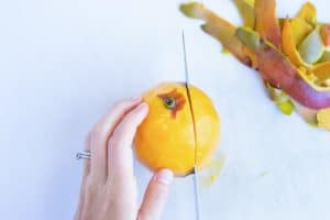 A hand holding a mango firmly while cutting it in half.