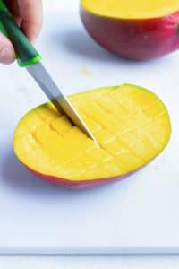 Making cuts into a mango flesh with a paring knife to create a grid.